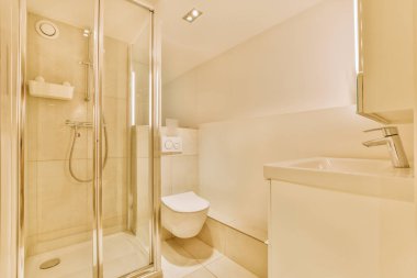 Çağdaş dairenin küçük fayanslı banyosunda lavabo ve duş arasında bulunan sifon tuvaleti