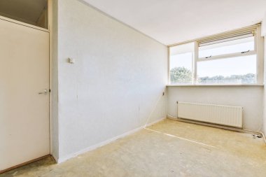 Evdeki boş ışık odasında, beyaz duvardaki plastik pencere ve radyatör.