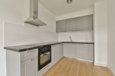 Pencereleri ve ahşap parke zemini olan boş beyaz mutfağın içi.