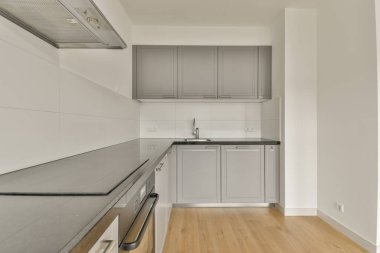 Pencereleri ve ahşap parke zemini olan boş beyaz mutfağın içi.