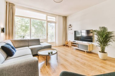 Çağdaş dairenin pencerelerine karşı rahat kanepesi ve televizyonu olan oturma odası.