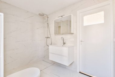 Modern flush toilet,shower box and ceramic sink installed on white tiled walls near mirror and towel in small restroom at home