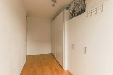 Modern dolap ve portmanto, beyaz duvarları ve parke zemini olan ferah odanın kapılarının yanında.