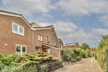 Boş bir kaldırım sokağından arabalı, ağaçlı tuğlalı evler manzarası.