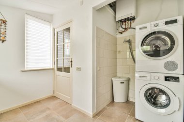 Beyaz duvarlı, karanlık zemini ve çamaşır makinesini yansıtan modern, parlak çamaşır odasının içi.