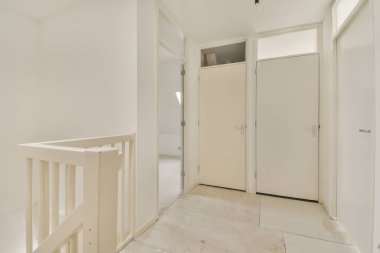 Kapalı beyaz oda kapısı çerçeveli resimlerin yanında ve evdeki merdivenin tepesinde şık bir lamba var.