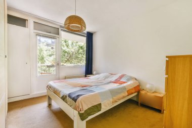 Küçük yatak odasının minimalist iç tasarımı. Köşesinde yumuşak yatak, ahşap gardırop ve lamba aydınlatmalı raflar var.