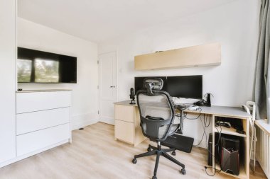 Modern apartmandaki hafif iş yerinde bilgisayar monitörleri ve beyaz tahtanın olduğu masanın yanına konforlu sandalye