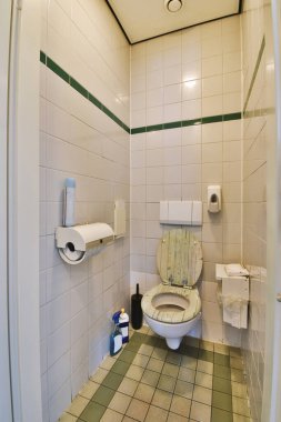 Duvarı duvara asılmış, beyaz duvarları ve kareli zemini olan dar tuvaletin içi.