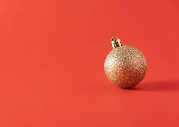 Kırmızı arka planda altın bir Noel topu. Yeni yıl kavramı