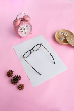 Cat's eye glasses in the photo from above with a minimalist concept on a purple paper background with an alarm clock decoration and dry leave