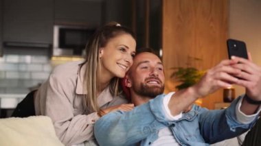 Evde yaşayan mutlu beyaz çift hücresel cihazda selfie çekiyor.