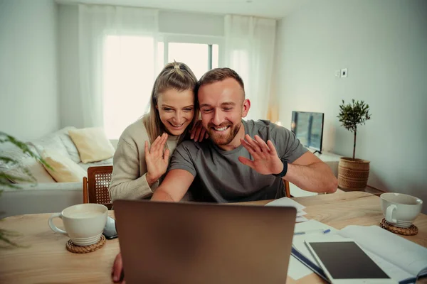 白种人快乐的一对夫妇坐在客厅里，一边和家人在电视上聊天一边对着笔记本电脑挥手 — 图库照片