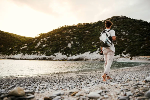 Blanke man wandelen langs het strand met rugzak bij zonsopgang — Stockfoto