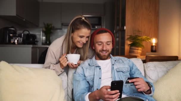 Feliz pareja caucásica sentada en el sofá bebiendo café caliente mientras toma selfies en el dispositivo celular — Vídeos de Stock