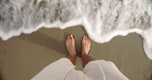 Кавказький самець стоїть на пляжі з ногами у воді. — стокове відео