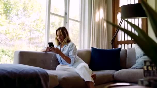 Biała kobieta relaksuje się na kanapie, pisząc na urządzeniu komórkowym — Wideo stockowe