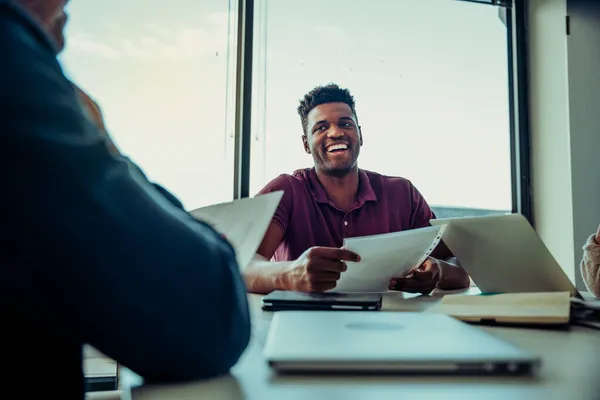 Männlicher Arbeiter lacht mit Chef und Klienten, die während der Besprechung im Sitzungssaal sitzen — Stockfoto
