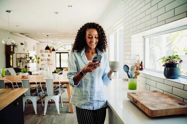 Donna che chatta sul cellulare in piedi in cucina con tazza di caffè — Foto Stock