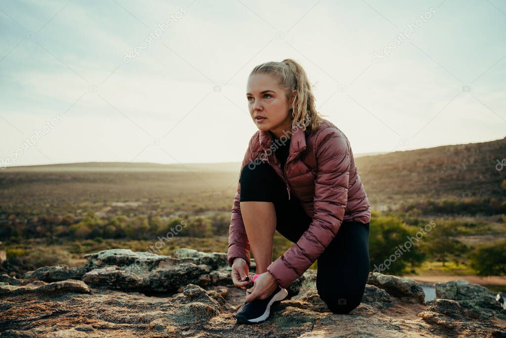 Caucasian female athlete tying shoe lace while hiking on mountain trail at sunset