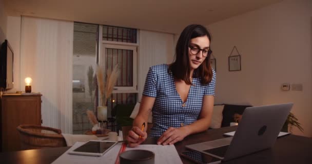 Mujer caucásica trabajando desde casa escribiendo en el ordenador portátil anotando información — Vídeo de stock