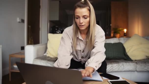 Feliz mujer caucásica trabajando desde casa escribiendo en el ordenador portátil sentado en el sofá — Vídeos de Stock