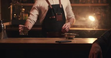 Barın arkasında duran beyaz erkek barmen erkek müşteriye içki hazırlıyor.