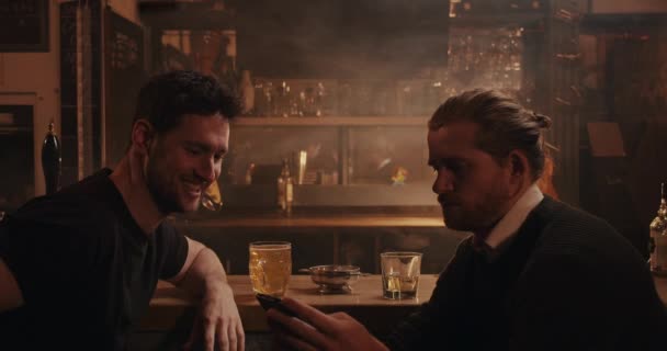 Cliente masculino caucasiano sentado no balcão do bar olhando para o dispositivo celular enquanto toma uma bebida — Vídeo de Stock