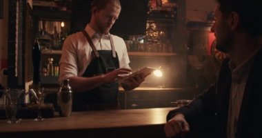 Beyaz erkek barmen, erkek müşteriyle uğraşırken dijital tabletle yazı yazıyor.