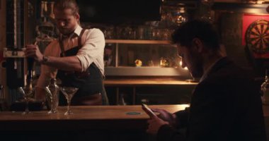 Beyaz erkek barmen cep telefonuyla müşteri mesajlaşması için içki hazırlıyor. 