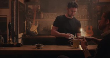 Beyaz erkek barmen, barın arkasındaki müşteriye içki hazırlıyor.