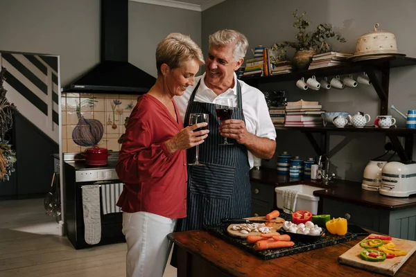 Casal de idosos caucasianos abraçando enquanto cozinha na cozinha — Fotografia de Stock