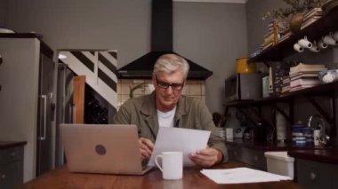 Beyaz, yaşlı bir erkek mutfakta evrak işleriyle uğraşıyor. 