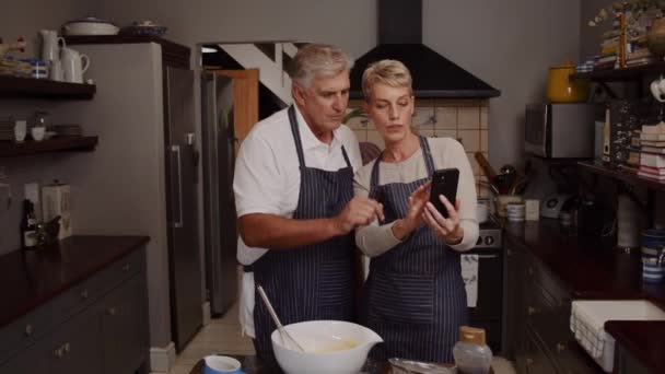 Pareja de ancianos horneando en la cocina con dispositivo celular — Vídeos de Stock