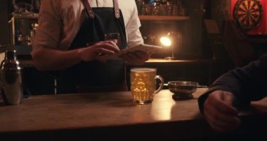 Barmen siparişini tamamlarken beyaz erkek müşteri barda tek başına oturuyor.
