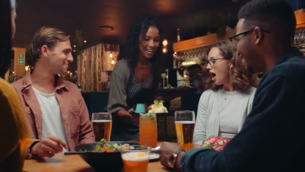 Vielfältige Freundesgruppe isst im Restaurant, während Kellnerin Essen ausliefert — Stockvideo