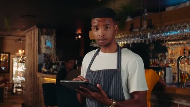 アフリカ系アメリカ人のウェイターがタブレットでレストランで働いています — ストック動画