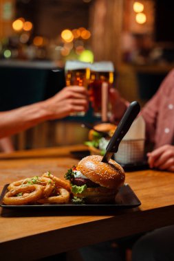 Dostlar akşam yemeği için dışarıda lezzetli peynirli burger ve soğan halkaları yiyorlar. 