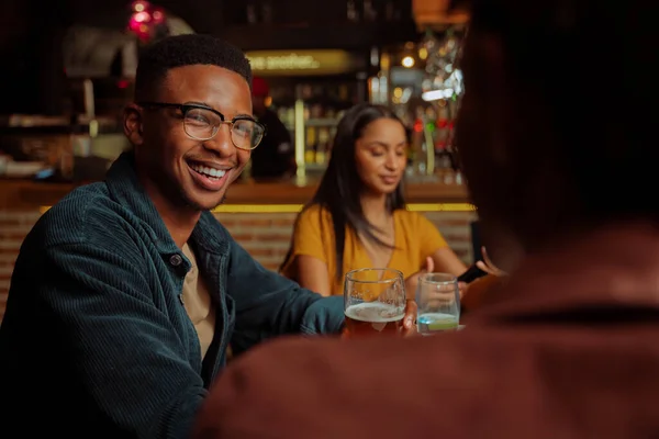 Hombre afroamericano sonriendo mientras disfruta del tiempo con amigos en el restaurante — Foto de Stock