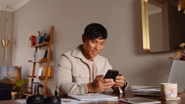 Asyalı erkek evde dizüstü bilgisayarla çalışırken mesajlaşıyor. — Stok video