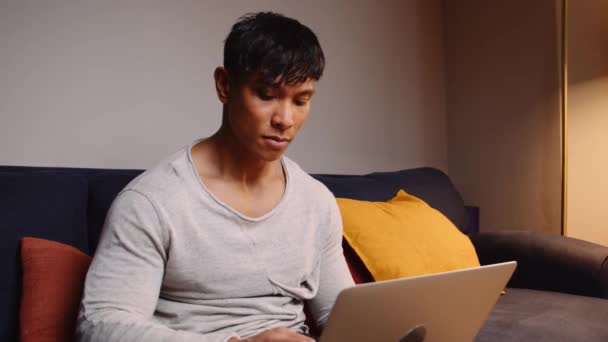 把坐在沙发上的亚洲男人关起来 在他的笔记本电脑上打字 高质量的4K镜头 — 图库视频影像
