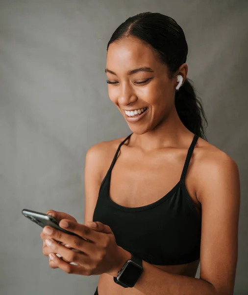 Close up African American female holding her cellphone in her hands and using her ear pods wearing her tank top . High quality photo