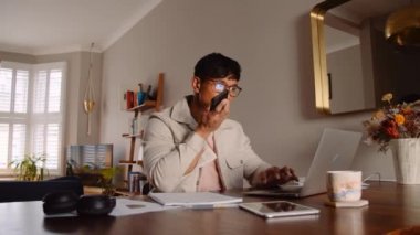 Asyalı adam dizüstü bilgisayarla meşgul ve cep telefonuna yüksek kaliteli 4K görüntüler bırakıyor.