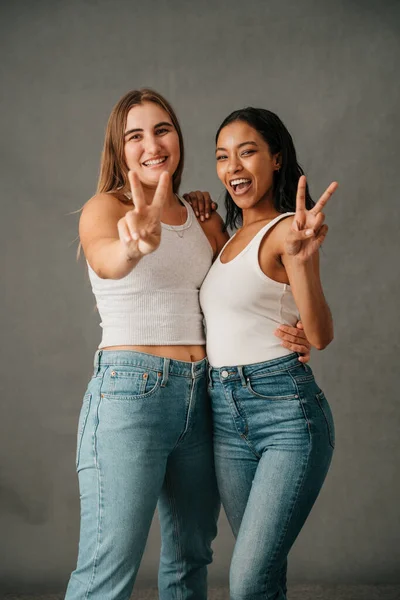 Two Girlfriends Smiling Showing Peace Sign Jeans Tank Tops Studio — 图库照片