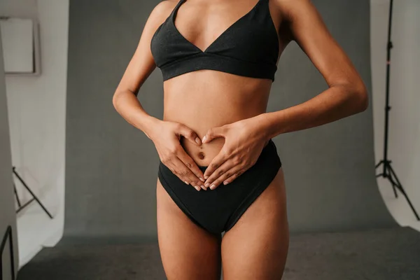 Afrika kökenli Amerikalı bir kadın, elleri karnının üzerinde, stüdyoda durarak kalp şekli oluşturuyor. Yüksek kalite fotoğraf