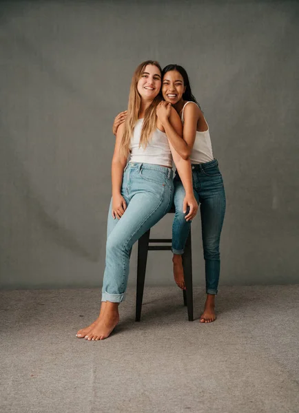 Casual girl friends bare foot and in there jeans sharing a stool and having fun in the studio. High quality photo