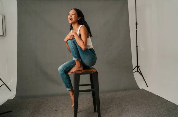 African American happily smiling sitting on a high stool bare foot in a studio. High quality photo