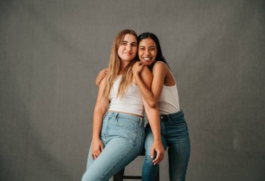 Girlfriends in there casual wear having fun sharing a high stool. High quality photo
