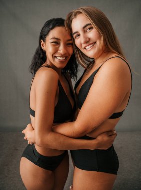  Portrait two happy smiling girlfriends standing in the studio and embracing in there underwear . High quality photo