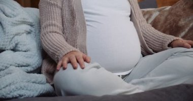 Pregnant woman sitting crossed legged on the sofa making heart shape with her hand on her tummy. High quality 4k footage